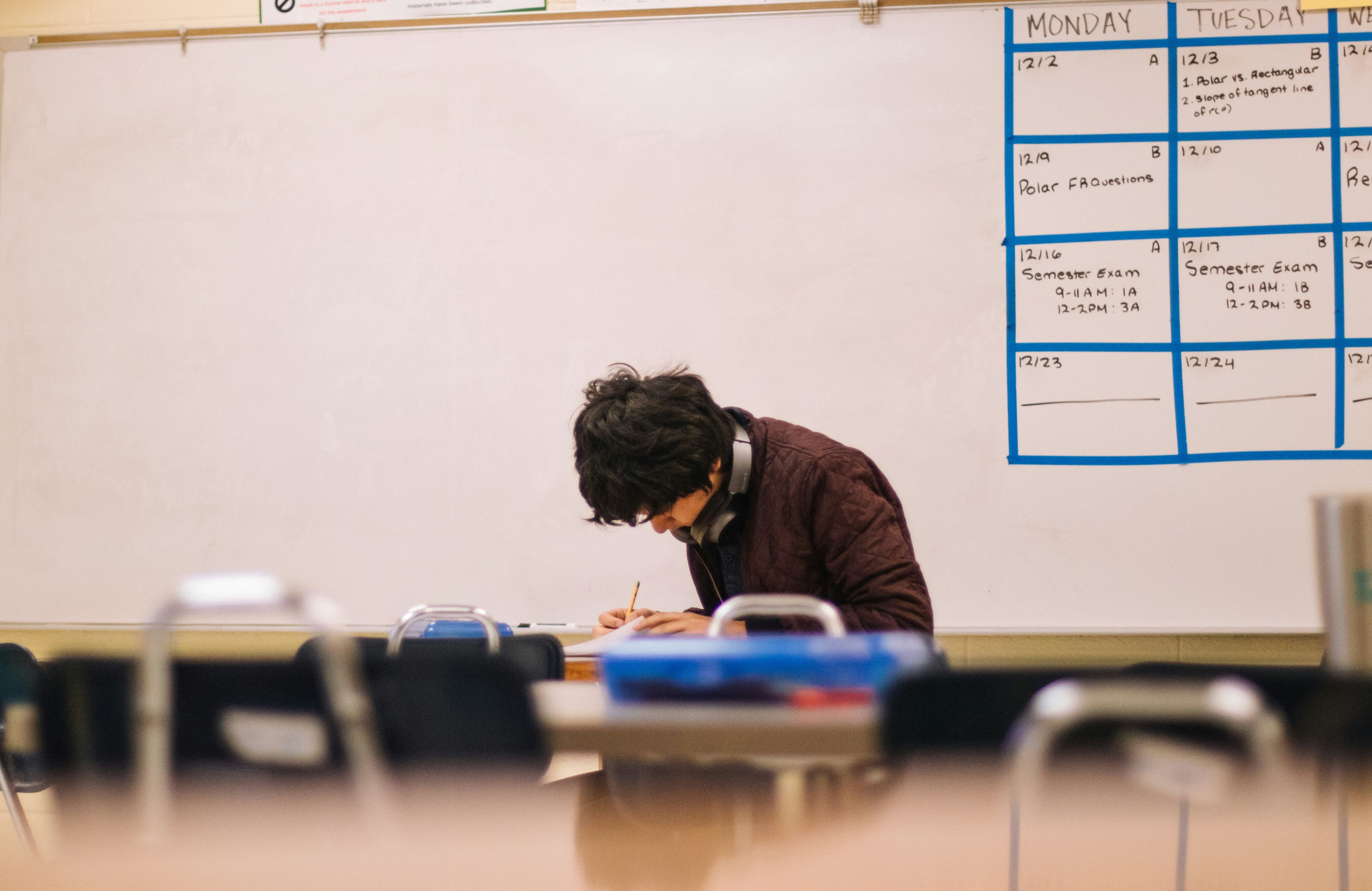 A student, wearing headphones around his neck, sits in a classroom.