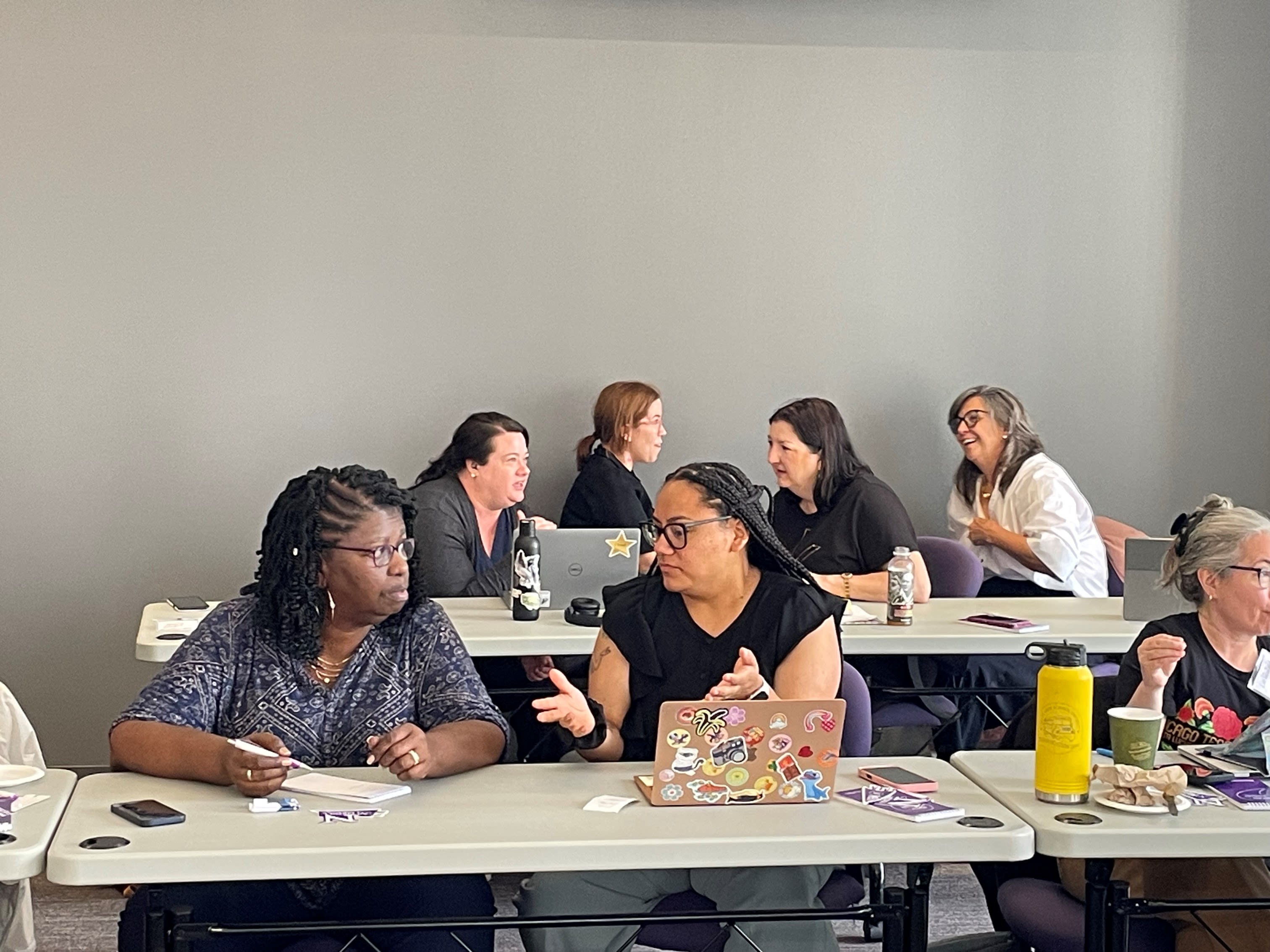 A handful of teachers sit at desks talking to one another