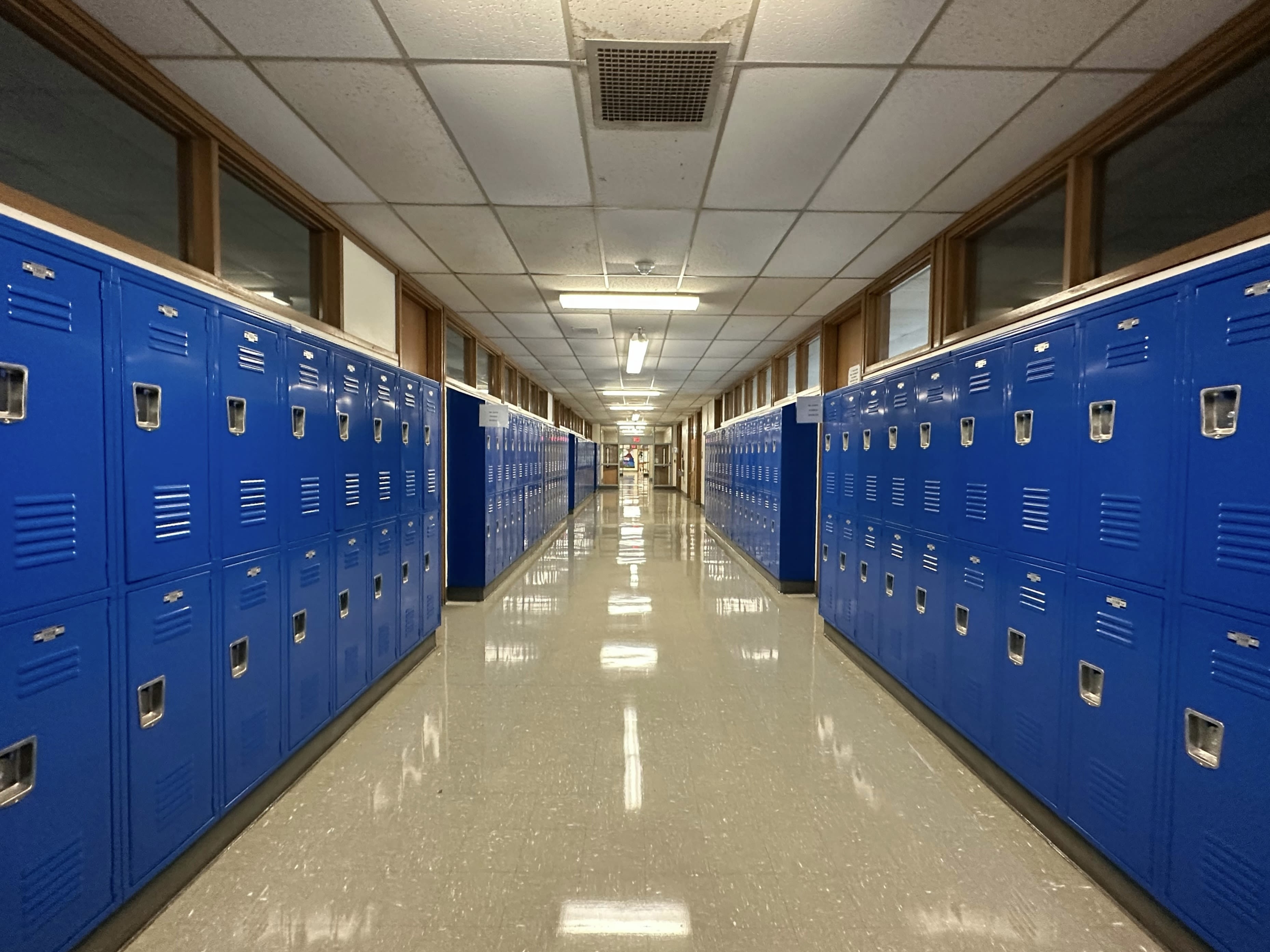A brightly-lit school hallway with blue lockers on both sides
