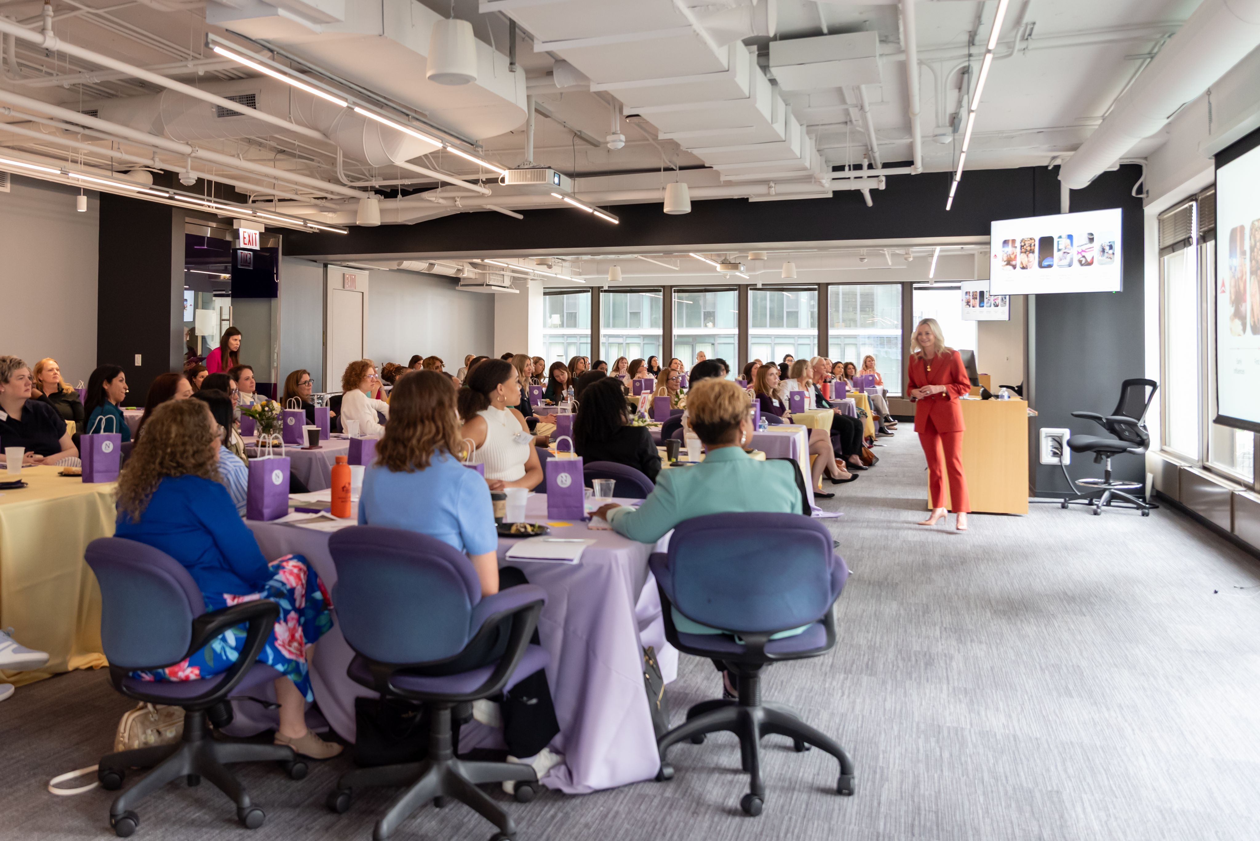 A person standing in a red suit gives a presentation to an audience