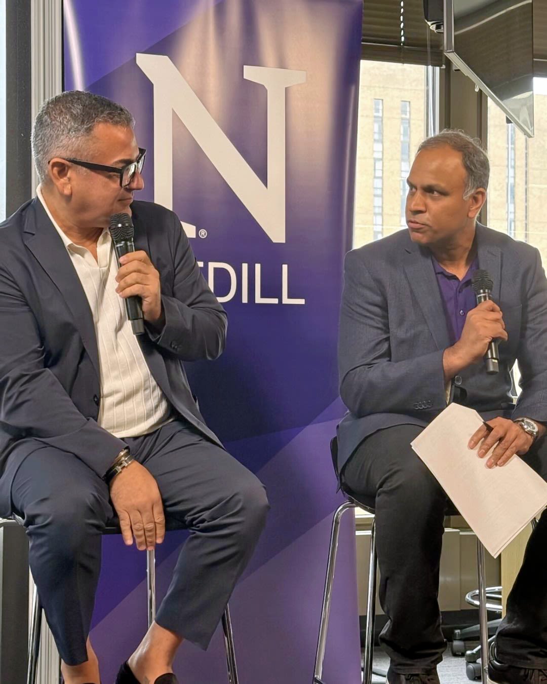 Two people dressed in suits talk to one another and hold microphones