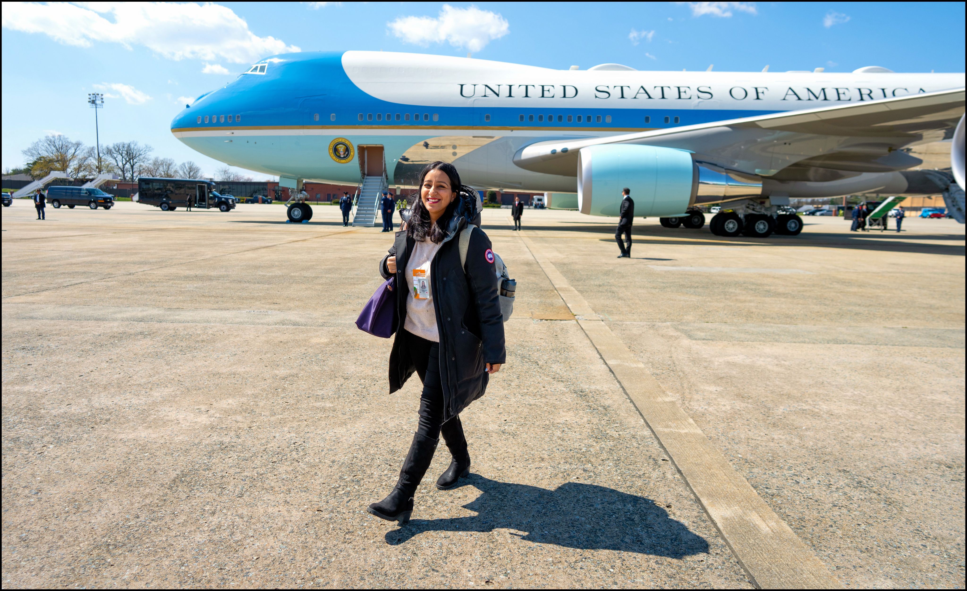 Sabrina Siddiqui smiles and carries a backpack while walking along an airport tarmac