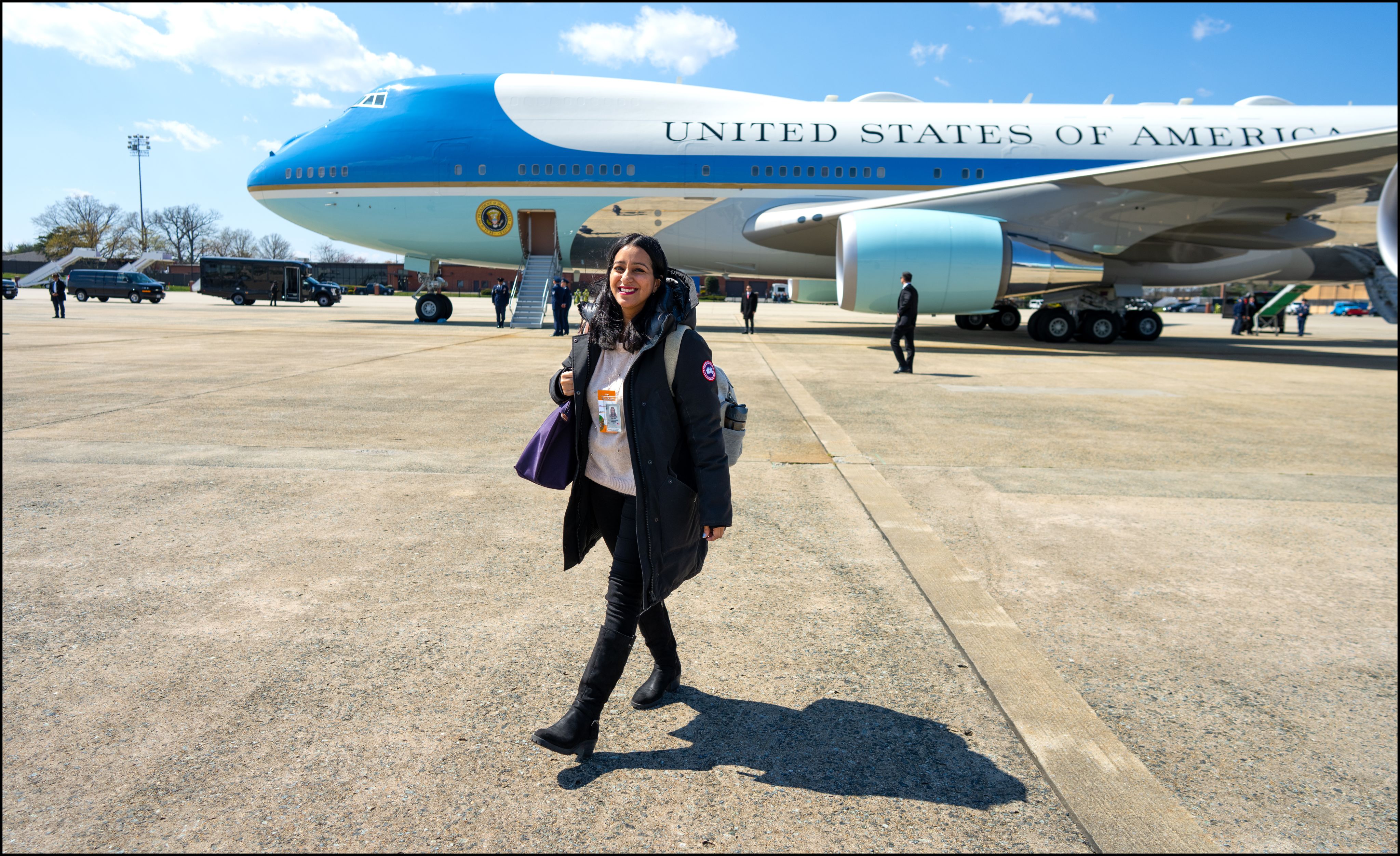 A person, Sabrina Siddiqui, in a coat walks in front of an airplane while both are on the tarmac