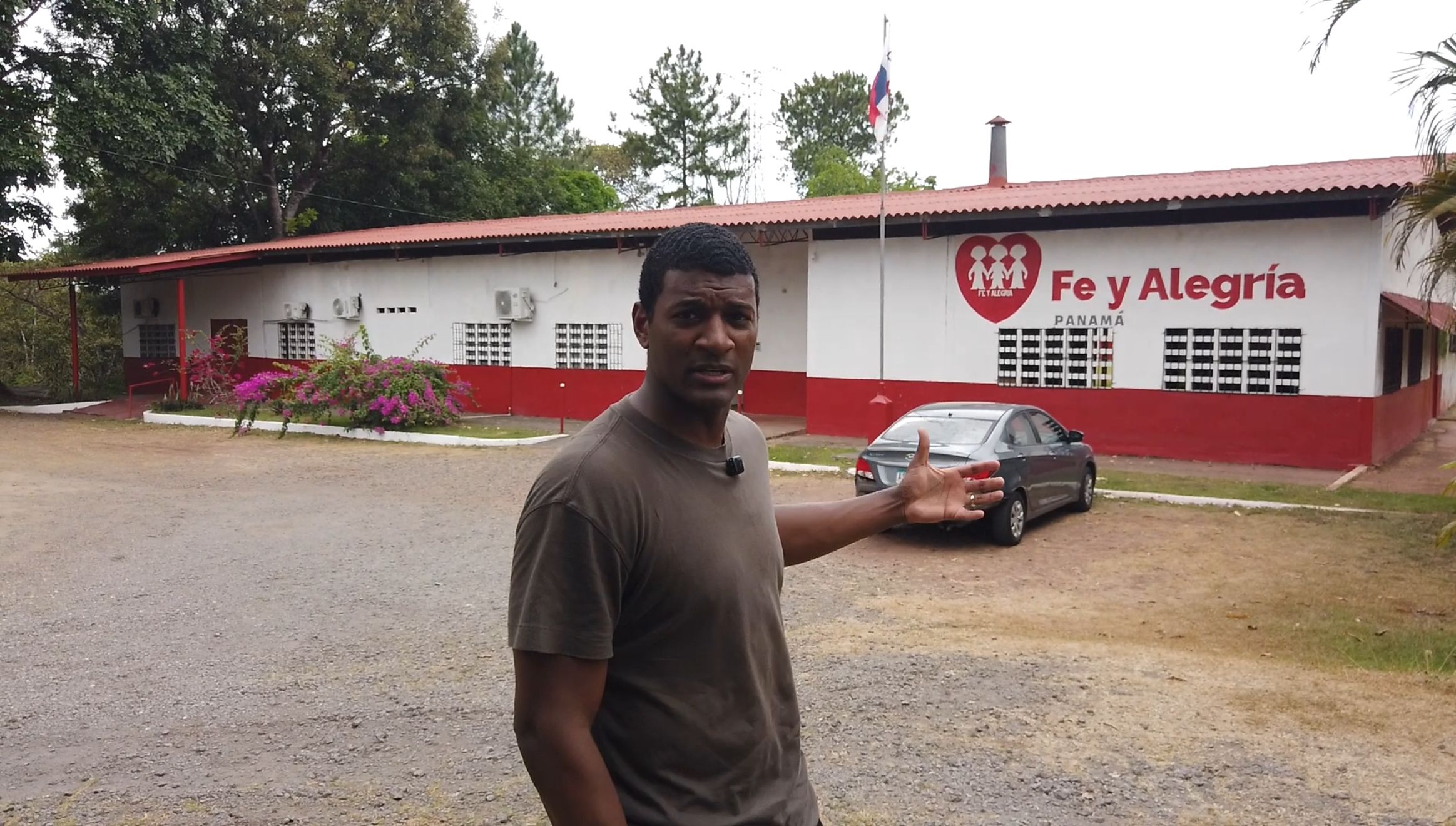 A person, Omar Jimenez, wearing a brown shirt walks and speaks while moving through a parking lot in front of a low building