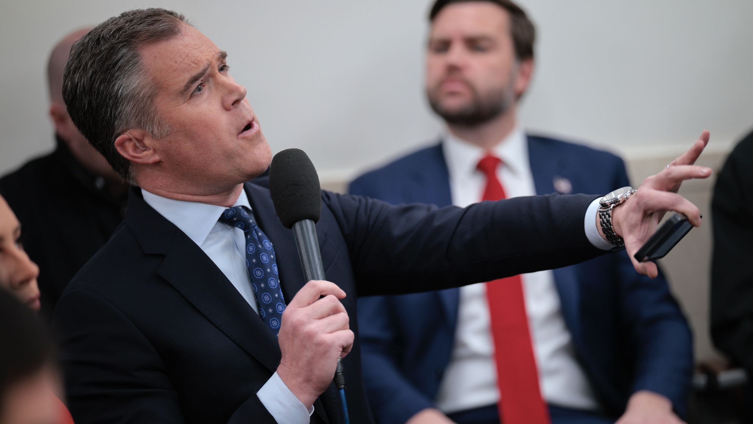 Peter Alexander holding a microphone extends his hand while speaking